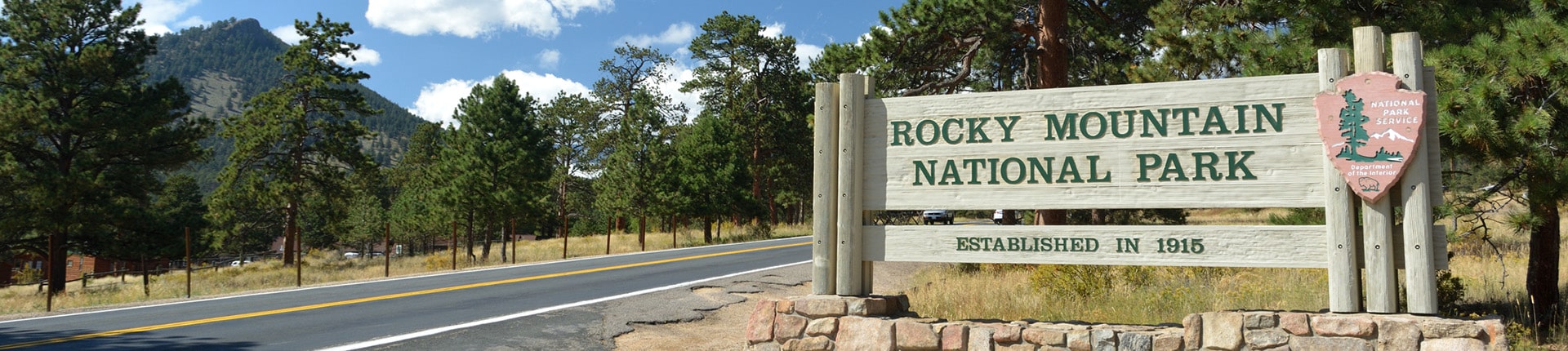 Sign for the Rocky Mountain National Park established in 1915 on the side of a road surrounded by trees