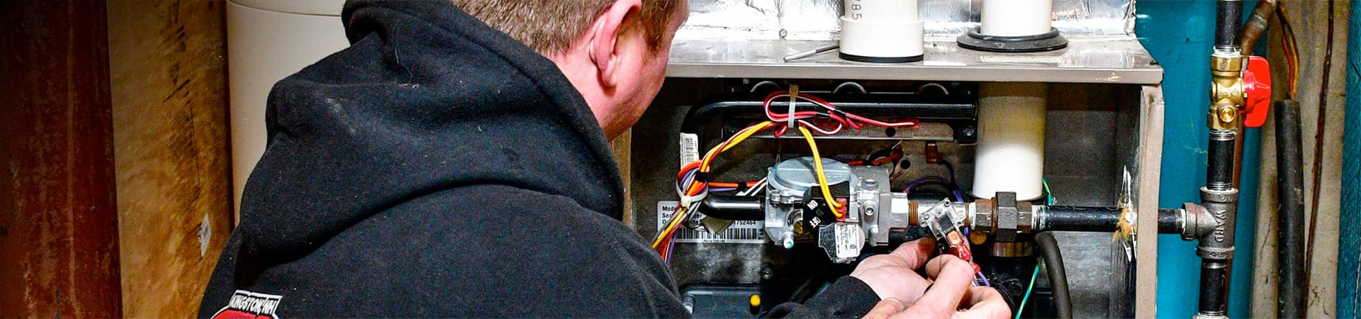 Plumber working on a gas furnace with the furnace door open and hands inside working.