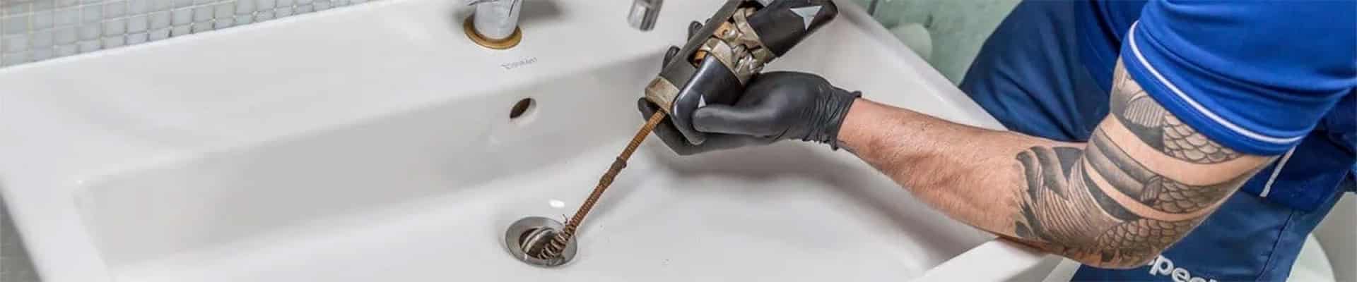 Technician with drain cleaning tools in hand and placed inside the drain hole of a bathroom sink