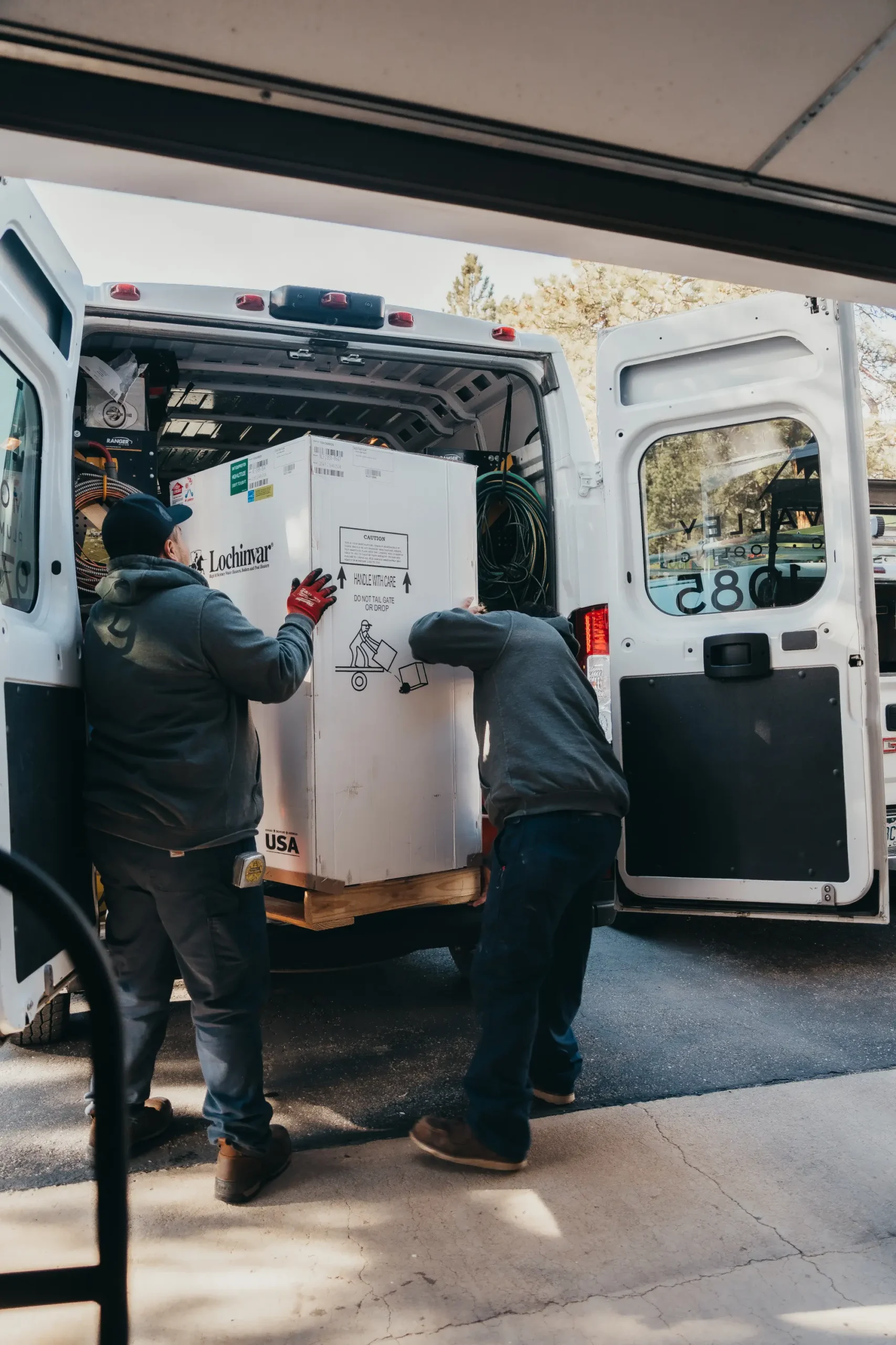 Workers loading large appliance into delivery van for transport