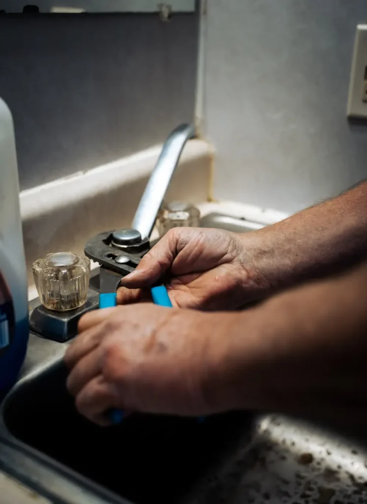 Plumber fixing kitchen faucet with wrench in dimly lit room